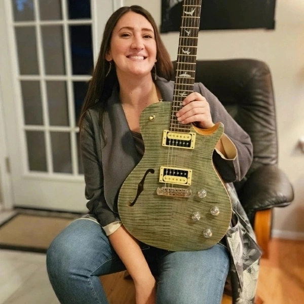 Bailey holding a green electric guitar for online music lessons